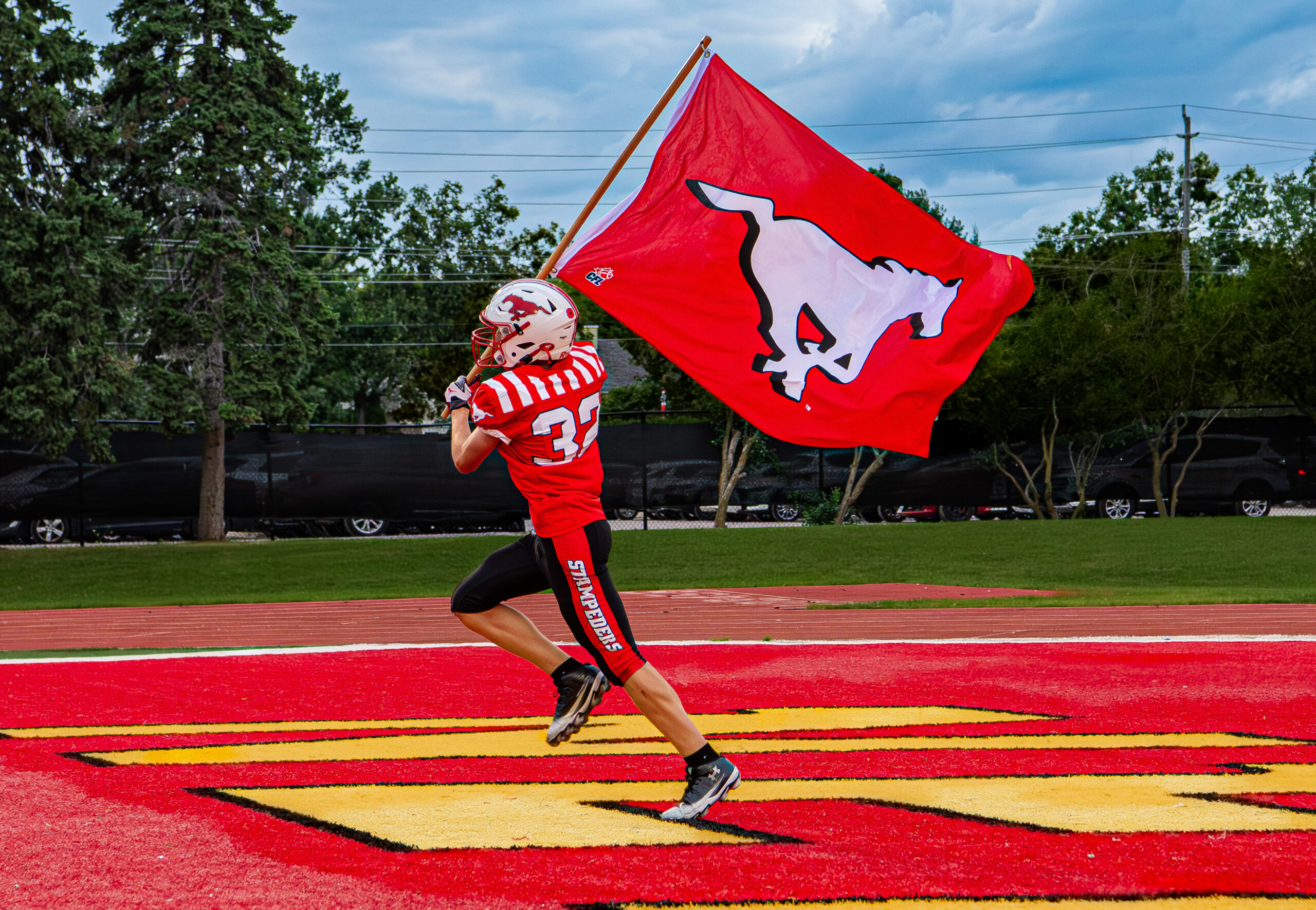 A Burlington Stampeders player runs with a large BMFA flag across the field.